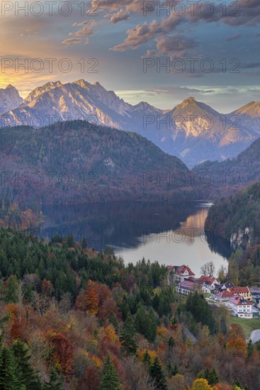 A picturesque view of a village nestled near a serene lake, surrounded by autumn foliage and the majestic Bavarian Alps at sunrise A perfect blend of nature and architecture