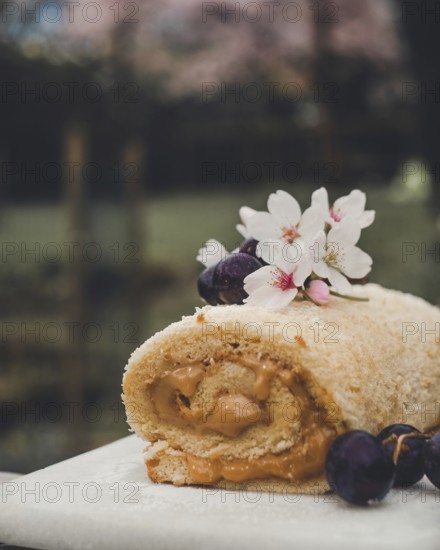 A close-up view of a Swiss roll filled with creamy dulce de leche, garnished with grapes, and cherry blossoms on a natural background