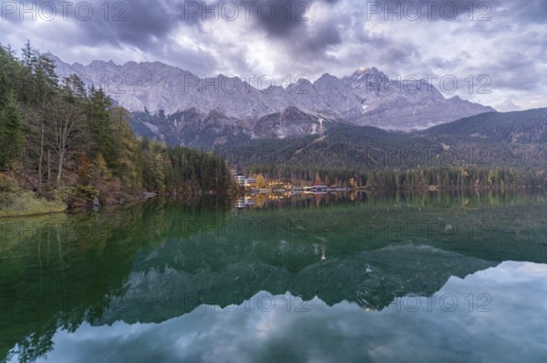 A breathtaking view of Eibsee at dusk, reflecting the towering Bavarian Alps and forested shoreline The tranquil waters and soft evening light create a serene alpine atmosphere