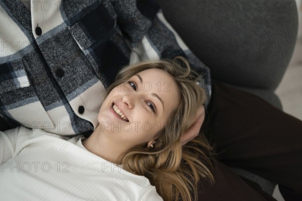 A young woman with a cheerful smile lying next to her cropped unrecognizable partner. She appears relaxed and happy in a casual setting at home looking at camera