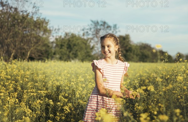 A young girl in a striped dress enjoys a peaceful moment in a blooming yellow flower field. She gently touches the petals, embracing nature, curiosity, and the beauty of childhood outdoors
