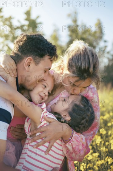 A loving family shares a heartfelt embrace surrounded by golden flowers in the countryside The parents and daughters express joy, affection, and deep emotional connection in nature