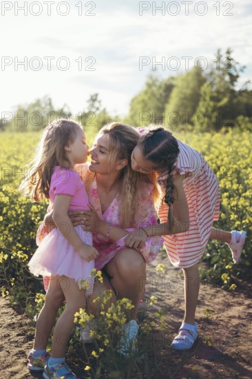 A loving mother kneels in a sunlit flower field as her daughters kiss her cheeks. This heartwarming scene captures affection, happiness, and the deep connection between mother and children