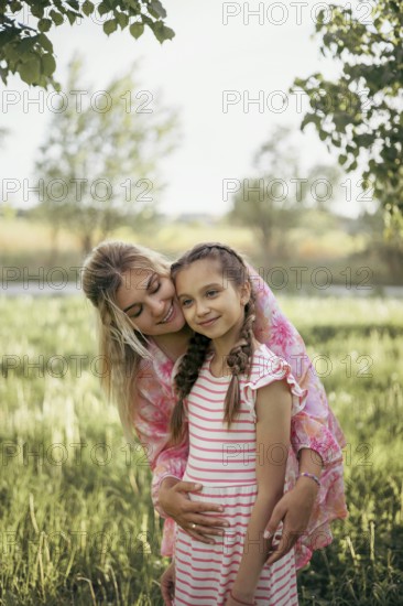 A mother gently embraces her daughter in a lush green field, radiating love and warmth Their smiles and closeness capture a tender family moment surrounded by nature's beauty
