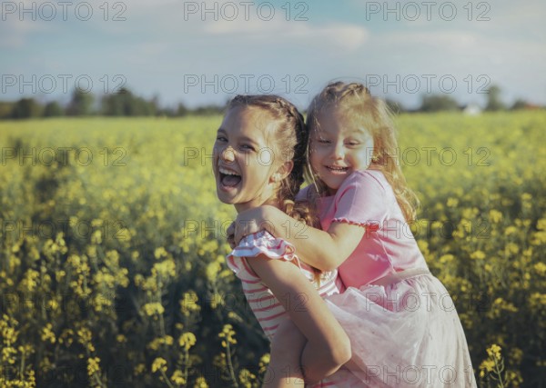 A young girl carries her little sister on her back as they laugh together in a field of bright yellow flowers Their joy and playfulness showcase the beauty of sibling love