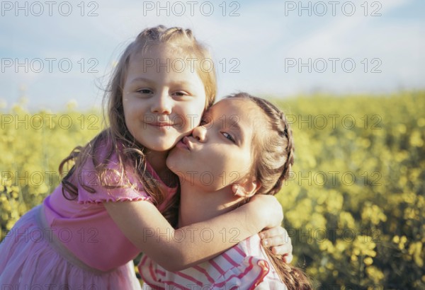 A sweet moment between two sisters as one gives the other a kiss on the cheek Their embrace captures the essence of childhood love and connection amidst nature