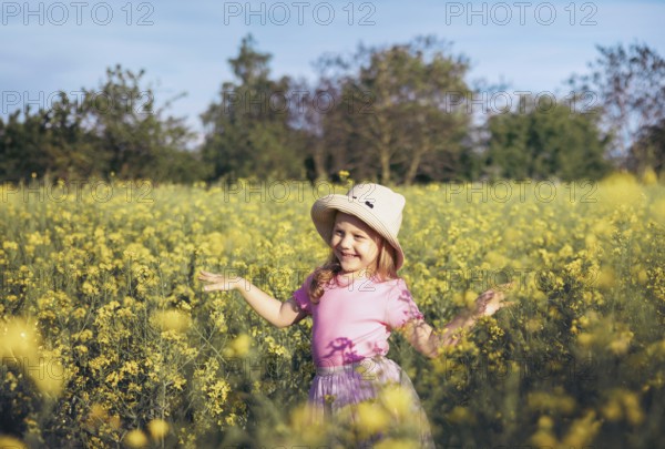 A little girl in a pink dress twirls happily among yellow flowers, embracing the beauty of nature and the freedom of childhood in the fresh countryside air