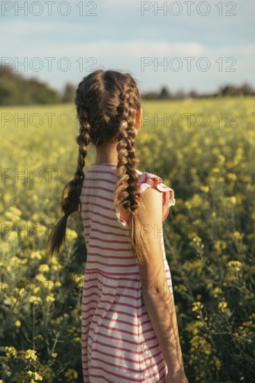 A young girl in a striped dress enjoys a moment of peace in a field of yellow flowers. Embrace nature, curiosity and the beauty of childhood outdoors