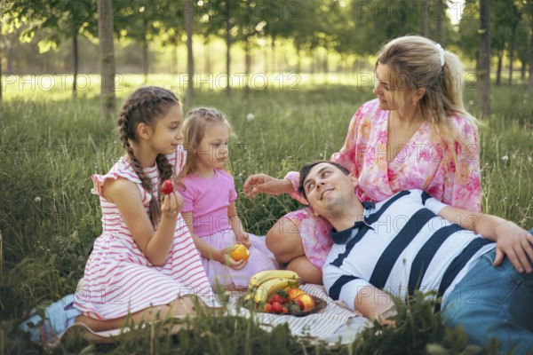 A loving family relaxes on the grass during a picnic, surrounded by nature. With fresh fruits and warm smiles, they share a joyful moment outdoors, embracing togetherness and happiness