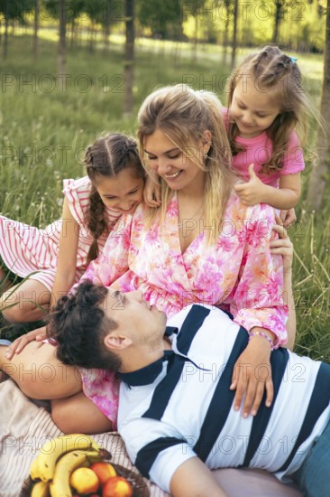 A loving family enjoys quality time together during a picnic in a peaceful green park. The parents and children share smiles, laughter, and warmth, creating a moment of pure happiness