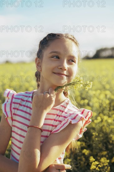 A young girl in a striped dress enjoys a peaceful moment in a blooming field, holding wildflowers and smiling as she basks in the warmth of the golden hour sunlight