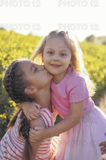 A sweet moment between two sisters as one gives the other a kiss on the cheek Their embrace captures the essence of childhood love and connection amidst nature
