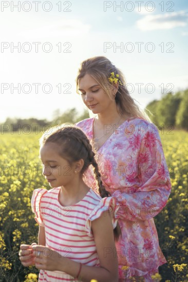 A mother and daughter spend quality time in a blooming yellow flower field, enjoying the warm sunset. The peaceful moment captures love, connection, and the beauty of nature