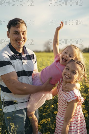 A young father and two daughters have fun together outdoors in the summer. Happy parenting and childhood