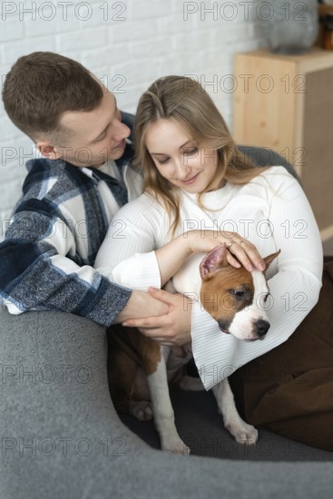 A young couple shares a tender moment with their small dog, conveying warmth and affection in a cozy home environment