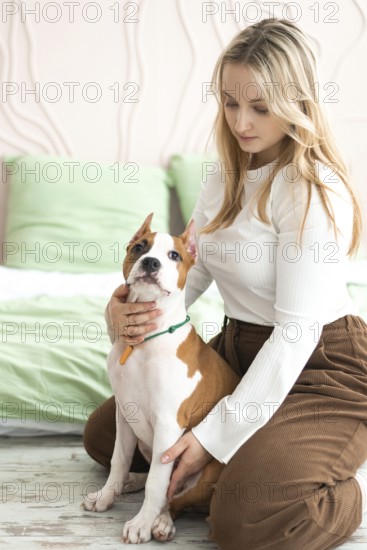A woman enjoys a quiet moment with her American Staffordshire Terrier in a serene, well-lit living room, demonstrating a close bond between pet and owner