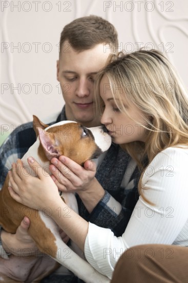 A man and woman affectionately interact with their brown and white dog in a cozy home setting, demonstrating a moment of love and care