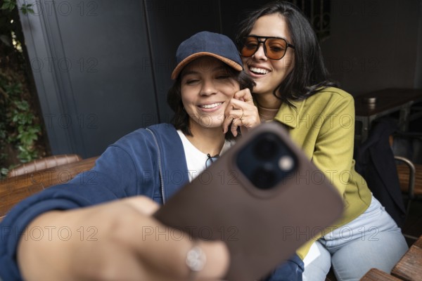 A lesbian couple is joyfully taking a selfie together outdoors, capturing their happiness and closeness. They are dressed casually, embodying a moment of love and companionship