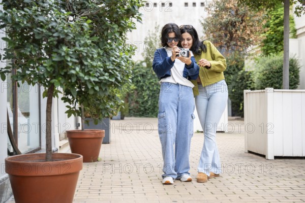 A joyful lesbian couple takes photos in a garden setting. They smile and explore the outdoors, creating cherished memories together with a camera in hand