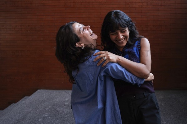 A joyful scene captures a multiethnic lesbian couple embracing and laughing together, celebrating their love and connection. Their happiness is palpable