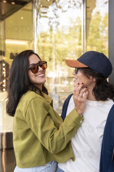 A lesbian couple shares a joyful moment in an urban setting. They wear casual outfits and sunglasses, exuding happiness and love under the soft daylight