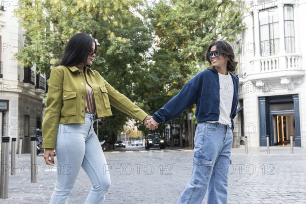 A lesbian couple enjoys a delightful walk hand-in-hand through a picturesque urban setting. They smile warmly at each other, radiating love and happiness