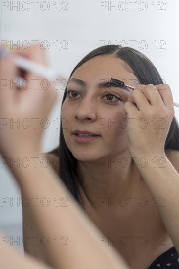 A woman concentrates while applying makeup using a brush in front of a mirror. The close up captures her focused expression and technique as she enhances her eyebrows