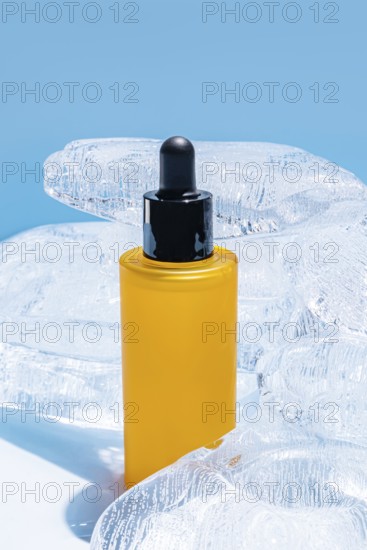 A vibrant yellow serum bottle with a black dropper, encased in clear ice blocks against a solid blue backdrop
