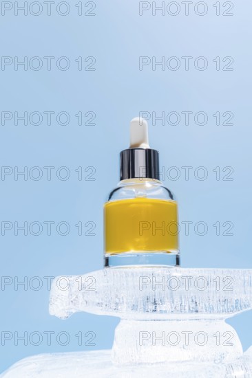 A cosmetic serum bottle with a dropper perched atop a block of ice, highlighted against a soft blue background, illustrating beauty product cooling