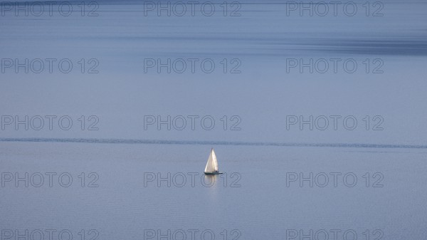A lone sailboat glides over Lake Geneva on a clear winter's day, framed by the vineyards of Lavaux and distant Alps