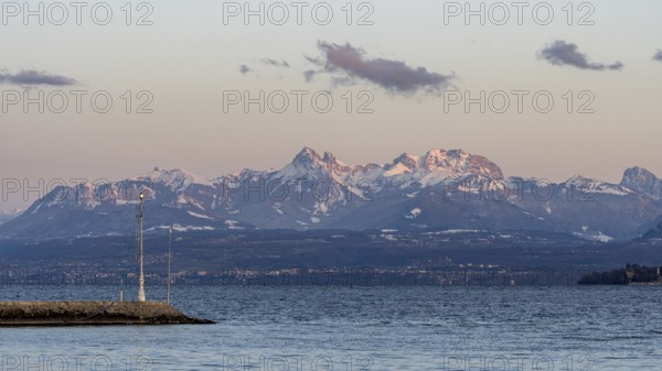 A breathtaking view of the snow-capped Swiss and French Alps seen from the shores of Lake Leman in Geneva. The tranquil water reflects the majestic mountains under a clear sky