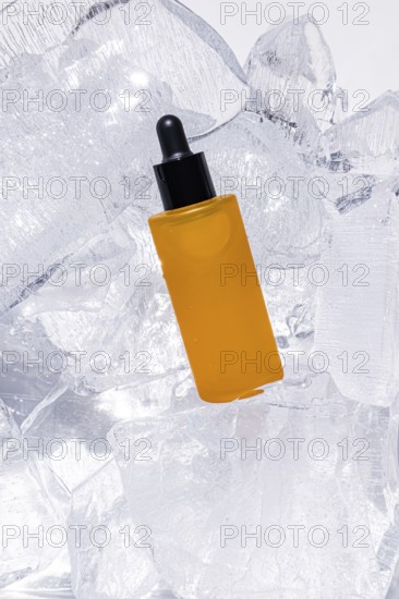 A vibrant, yellow serum bottle with a dropper, artfully encased in glistening ice cubes, emphasizing luxury and cool freshness in skincare packaging