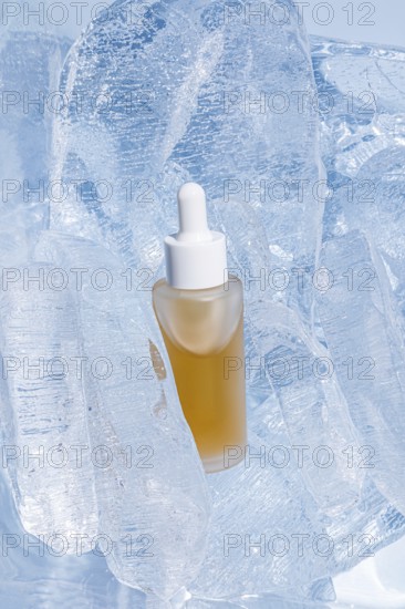 A clear serum bottle with a dropper, encapsulated by shimmering translucent ice cubes, stands out with its golden yellow content