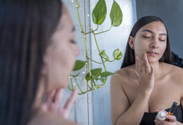 A woman applies skincare cream to her face in front of a mirror. She is focused on self care, with a relaxing atmosphere and natural lighting enhancing her beauty routine