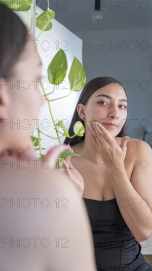 A woman is applying skincare cream while looking in the mirror. Surrounded by indoor plants, she is focused on her self care routine in a peaceful home environment