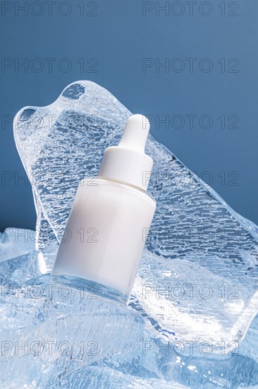 A serum bottle with a dropper rests on textured melting ice cubes against a blue background, conveying a sense of cool freshness