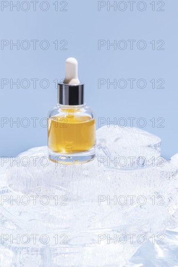 A single cosmetic serum bottle with a dropper cap, presented on a stack of clear ice cubes, under a light blue background
