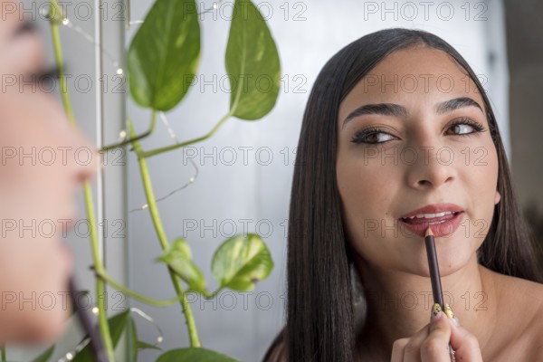 A woman applies lip liner while looking in a mirror, with lush green leaves in the background. The scene captures a serene and intimate moment in a beauty routine