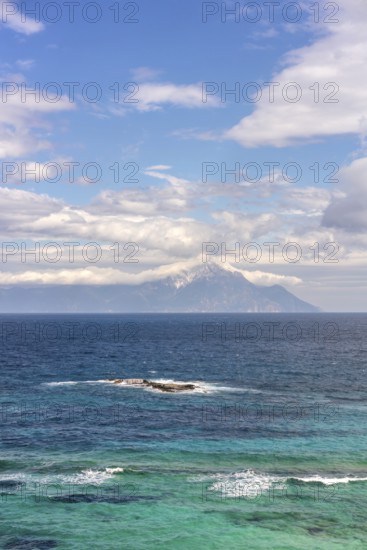 Captivating view of the Aegean Sea with vibrant blue and turquoise waters in Greece. Mount Athos rises majestically in the background under a partly cloudy sky