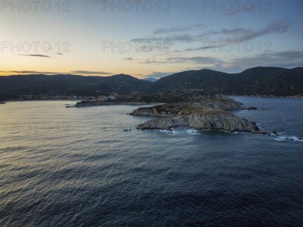 A scenic view of Kalamitsi village and beach in Greece at sunset. The rugged coastline, calm sea, and rolling hills create a peaceful and picturesque Mediterranean landscape