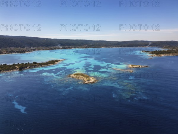 Drone view of Diaporos Island and Karydi Beach in Greece, showcasing crystal-clear turquoise waters, rocky islets, and lush greenery under a sunny sky. A stunning Mediterranean landscape