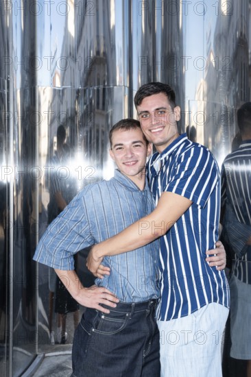 A smiling gay couple embraces in the lively streets of Madrid, reflecting the vibrant and inclusive spirit of the city. They enjoy a sunny day, surrounded by modern architecture