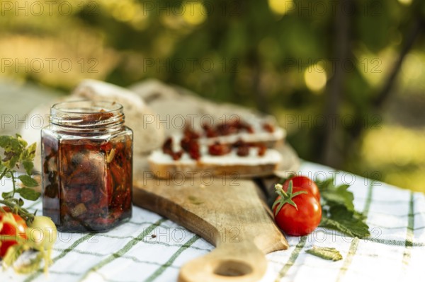 A rustic scene of canapes being prepared. Fresh tomatoes, a jar of preserved vegetables, and bread slices on a wooden board create a cozy culinary atmosphere