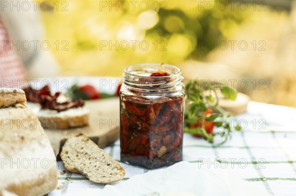 A rustic outdoor setting featuring a jar of homemade sun-dried tomatoes, fresh bread, and ripe tomatoes on a wooden board. The warm natural light enhances the farm-to-table aesthetic