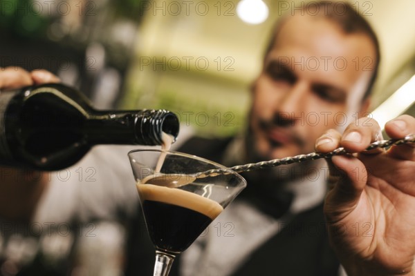 A skilled bartender expertly pours a drink into a glass, showcasing precision and flair. The vibrant cocktail bar ambiance highlights his professional expertise in mixology