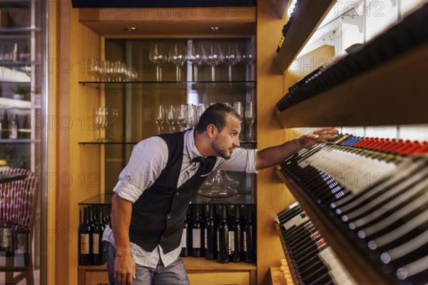 A professional sommelier meticulously selects wine bottles in a sophisticated cocktail bar, surrounded by neatly arranged glassware. Perfect ambiance for connoisseurs