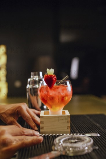 A professional bartender skillfully prepares a vibrant cocktail garnished with a fresh strawberry at a modern cocktail bar. The atmosphere is inviting and stylish