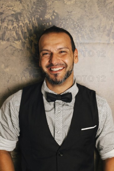 A professional bartender dressed stylishly with a bow tie, smiling warmly. The image captures the ambiance of a cocktail bar, reflecting hospitality and expertise