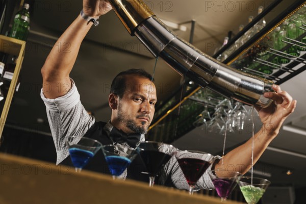 A professional bartender skillfully mixing vibrant cocktails in a stylish bar setting. The image captures the art and expertise of cocktail crafting with a focus on precision and color