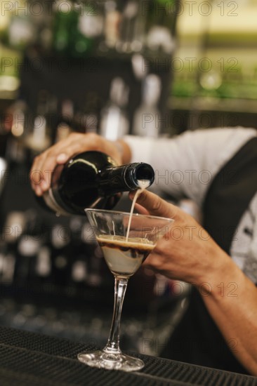 A professional bartender skillfully pours a creamy beverage into a martini glass at a modern cocktail bar, showcasing expertise and attention to detail